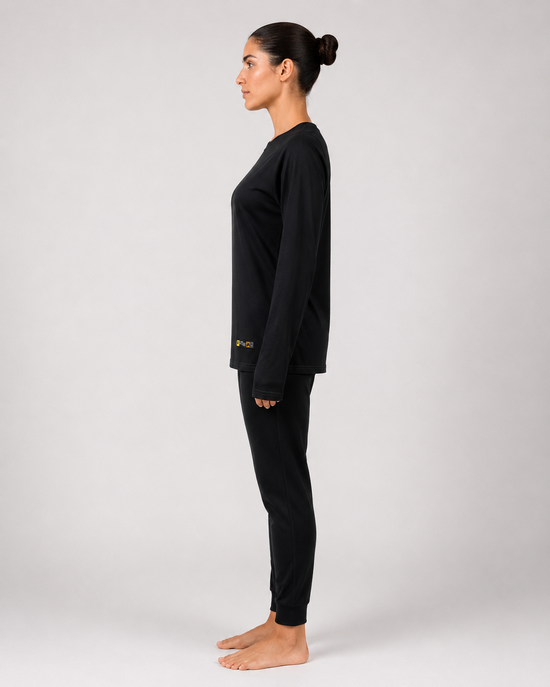 Primera capa ignífuga femenina confeccionada en jersey con camiseta de manga larga y pantalón negro, vista lateral izquierda.