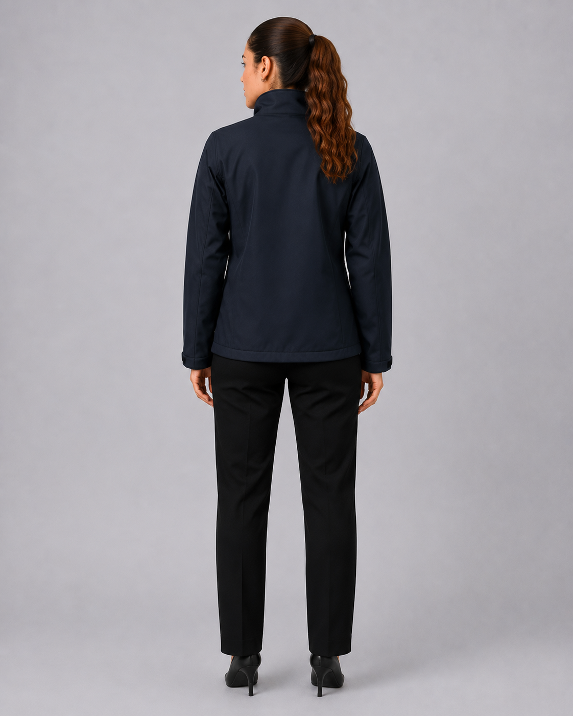 Parte posterior del uniforme corporativo femenino con chaqueta Softshell y pantalón ejecutivo negro, vista posterior.