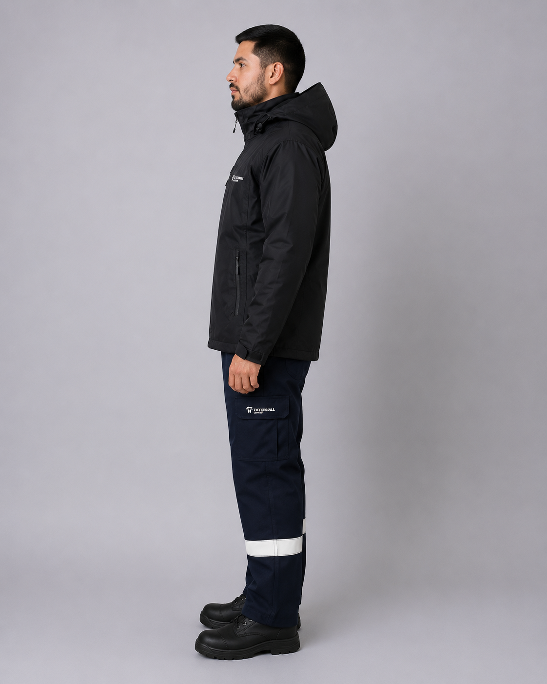 Uniforme operativo con parka negra de capucha, pantalón cargo con bandas reflectantes y bolsillos laterales, vista lateral izquierda.