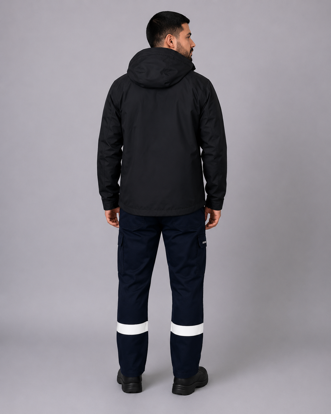 Parte posterior del uniforme corporativo con parka negra de capucha y pantalón cargo con bandas reflectantes en ambas piernas, vista posterior.