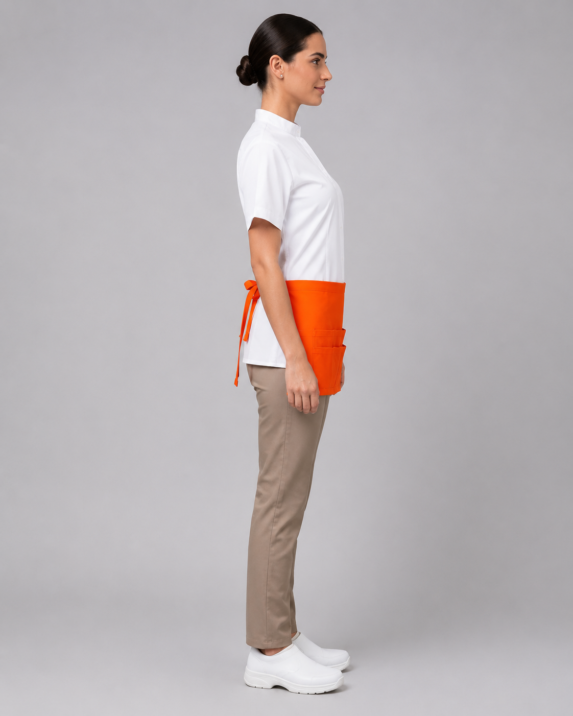 Uniforme para atención al cliente compuesto por blusa blanca, pantalón beige y delantal naranja de cintura con compartimientos, vista tres cuartos.