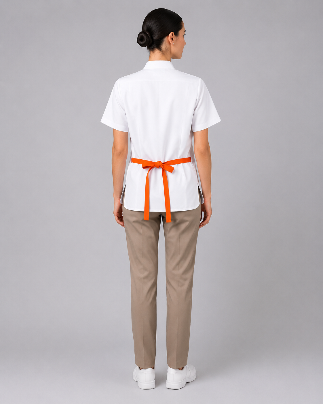 Parte posterior del uniforme corporativo con blusa blanca, pantalón beige y delantal de cintura ajustado mediante cintas, vista posterior.